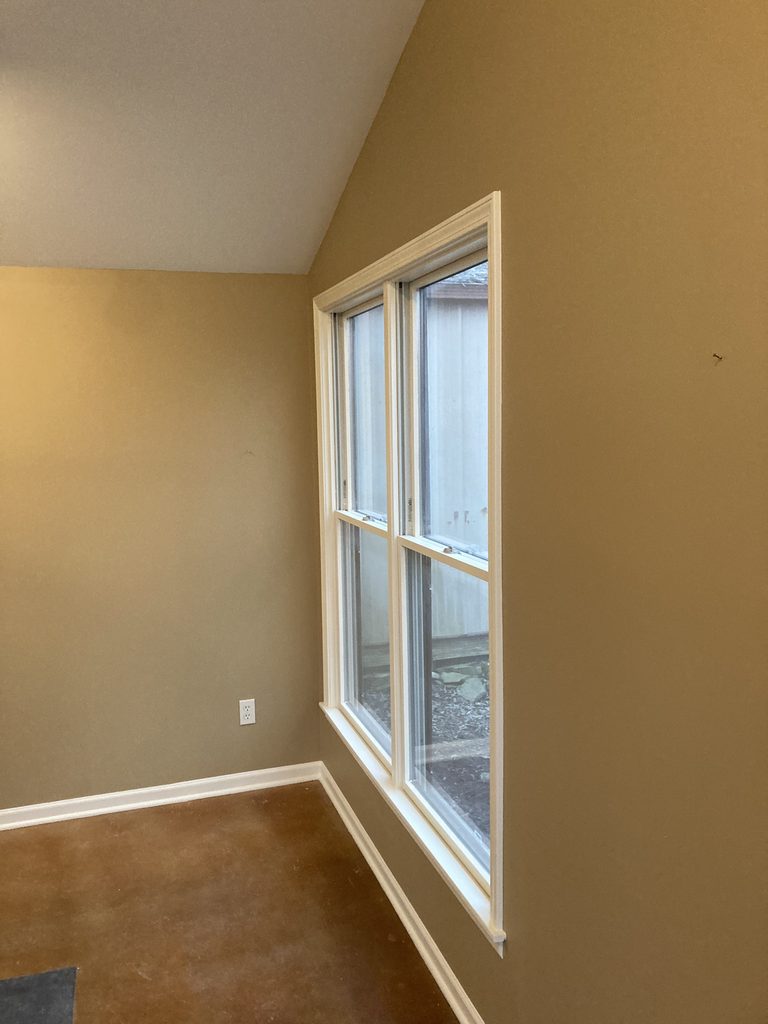Finished tall window with white trim against a freshly painted tan wall.
