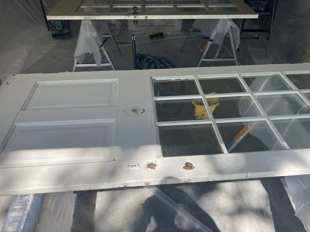 Primed white door resting on wooden sawhorses inside a plastic paint tent.