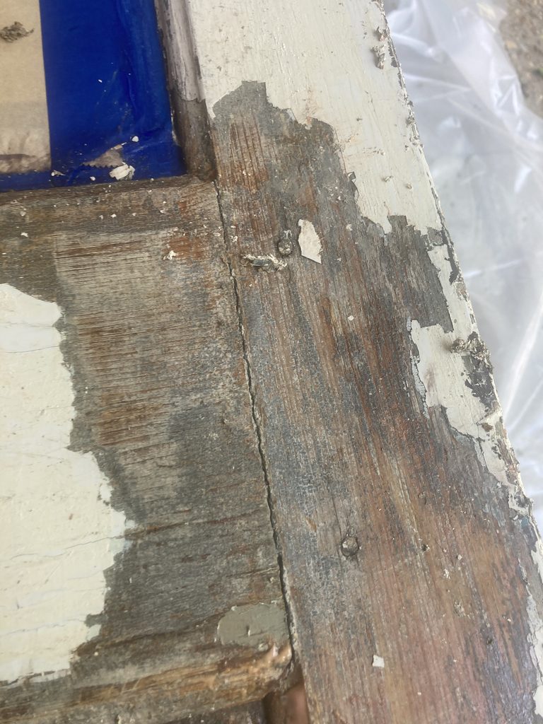 Close-up of peeling paint and exposed wood grain at a stripped door joint.