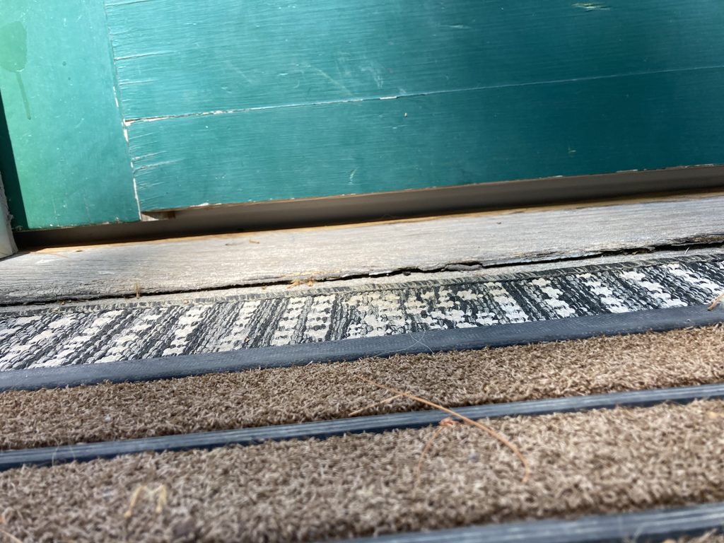 Close-up of a teal-painted door bottom meeting a worn wood threshold and door mat.