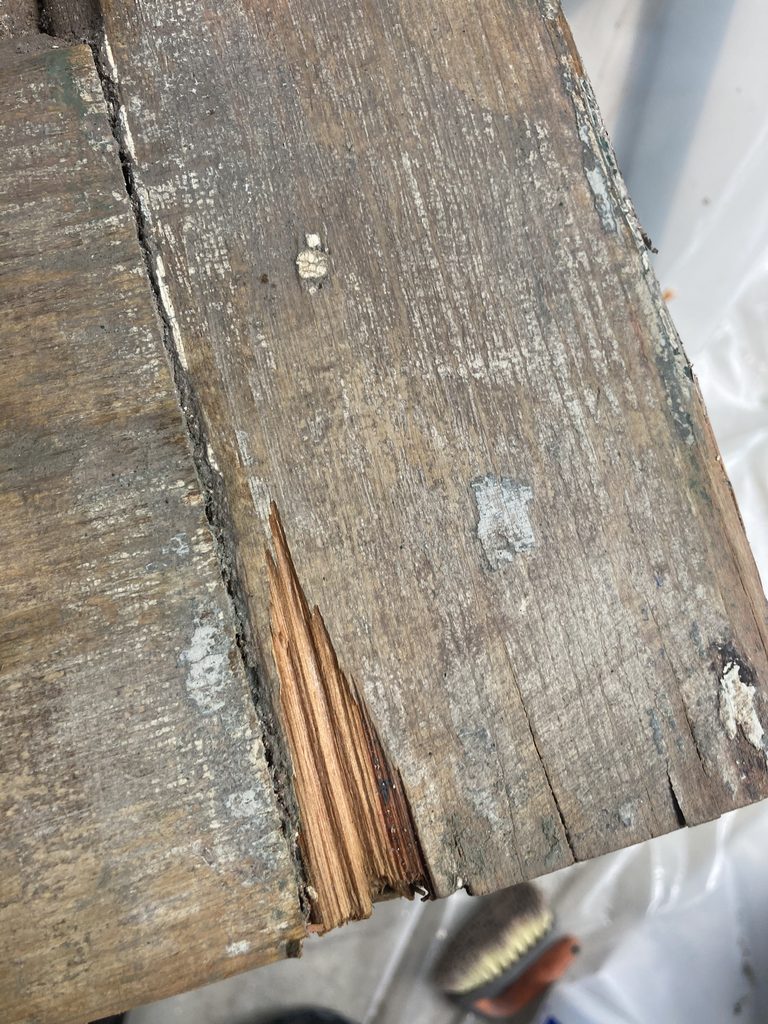 Close-up of bare wood grain and paint residue at a stripped door corner.