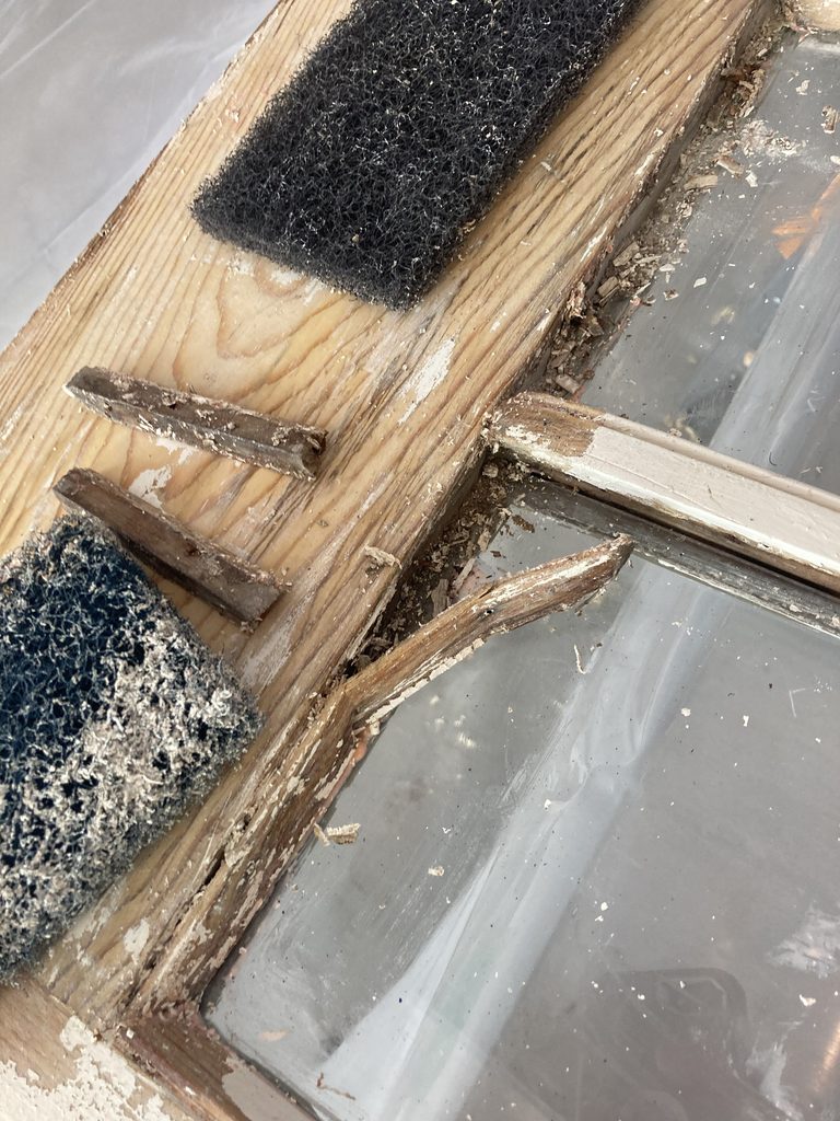 Sanding pad and small cut wood strips on a workbench next to a glazed sash bar.