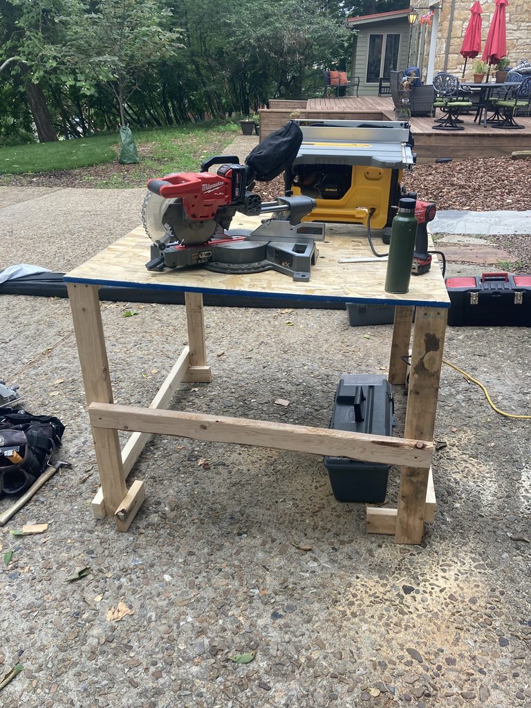 Outdoor plywood workbench holding a miter saw and a table saw.