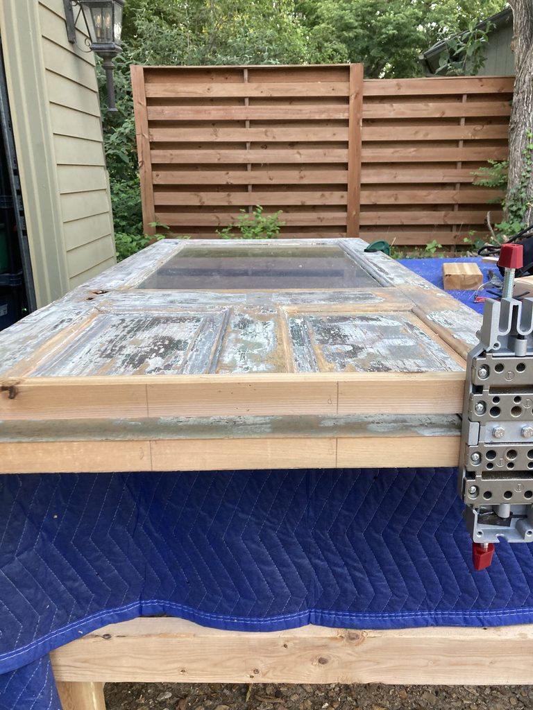 Stripped wood door frame with its glass panel propped against an outdoor cedar fence.