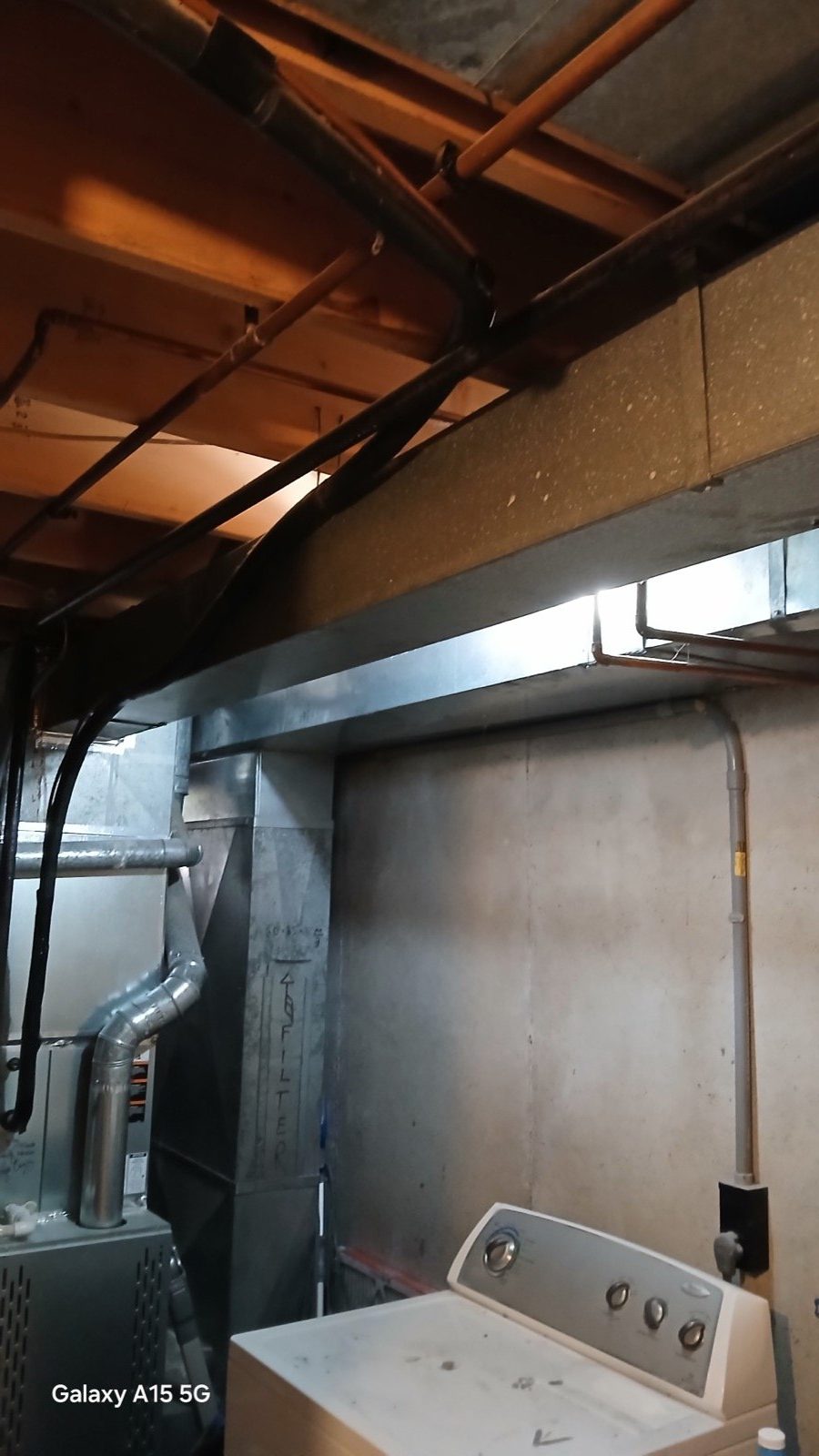 Exposed floor joists and HVAC ducts in unfinished basement ceiling before framing and drywall.