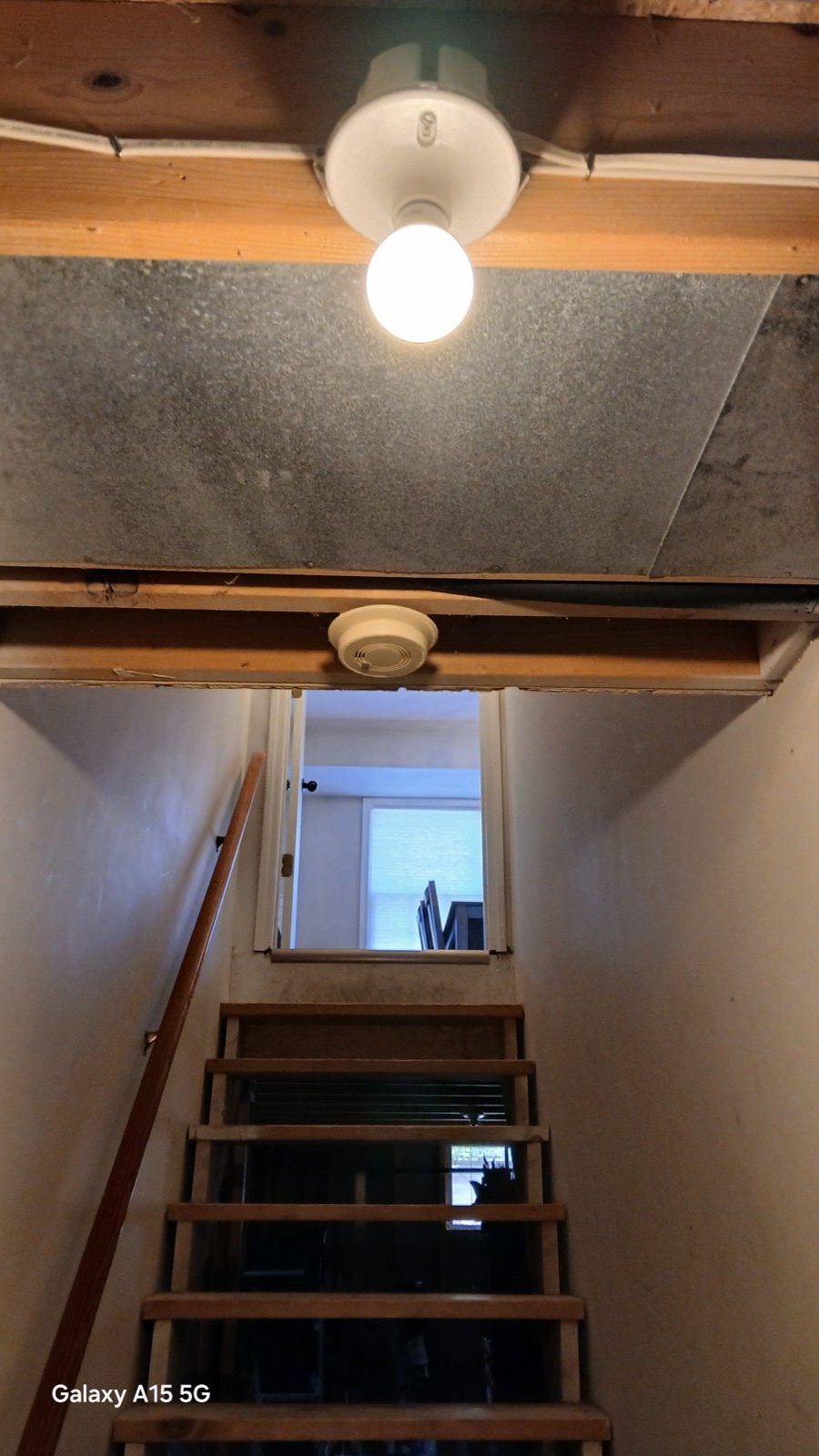 Partially framed basement room with bare light bulb and window before full framing and insulation.