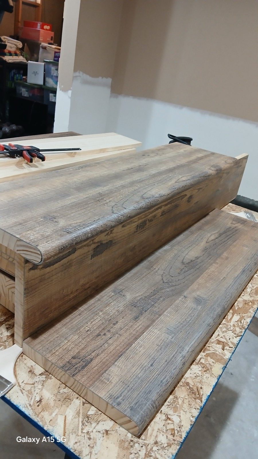 Reclaimed wood handrail clamped and glued at a workbench with staining supplies visible.