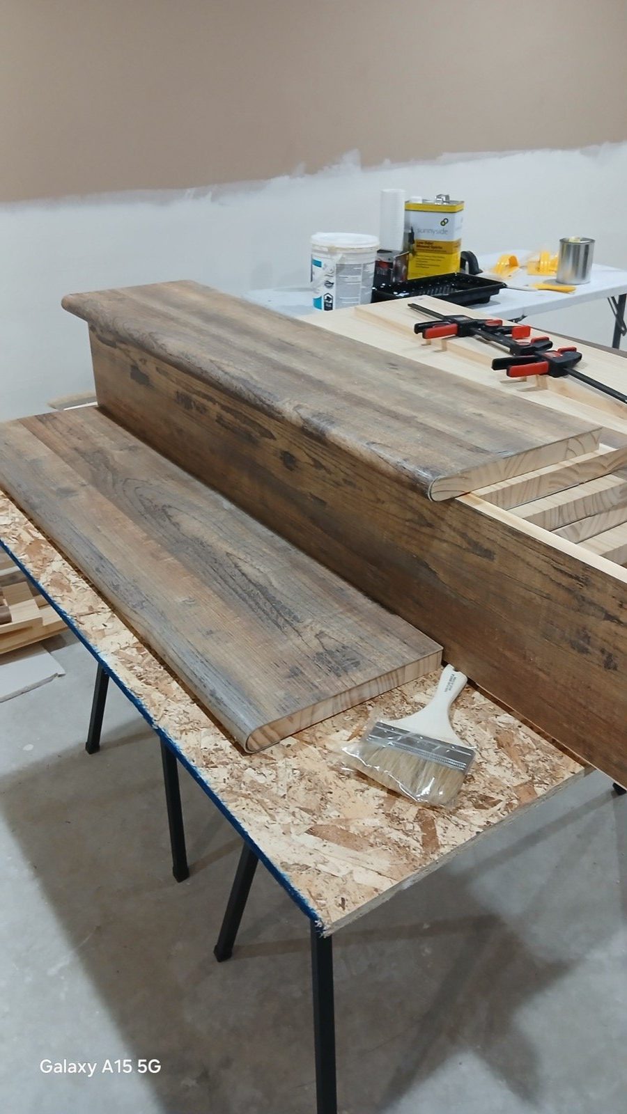 Stained reclaimed wood stair treads laid on sawhorses being prepared for installation.