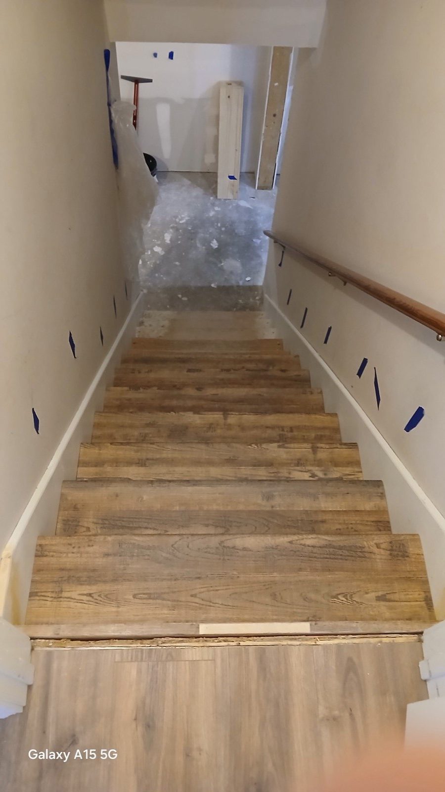 Rustic reclaimed wood baluster wall under construction with vinyl plank floor and stair soffit visible.