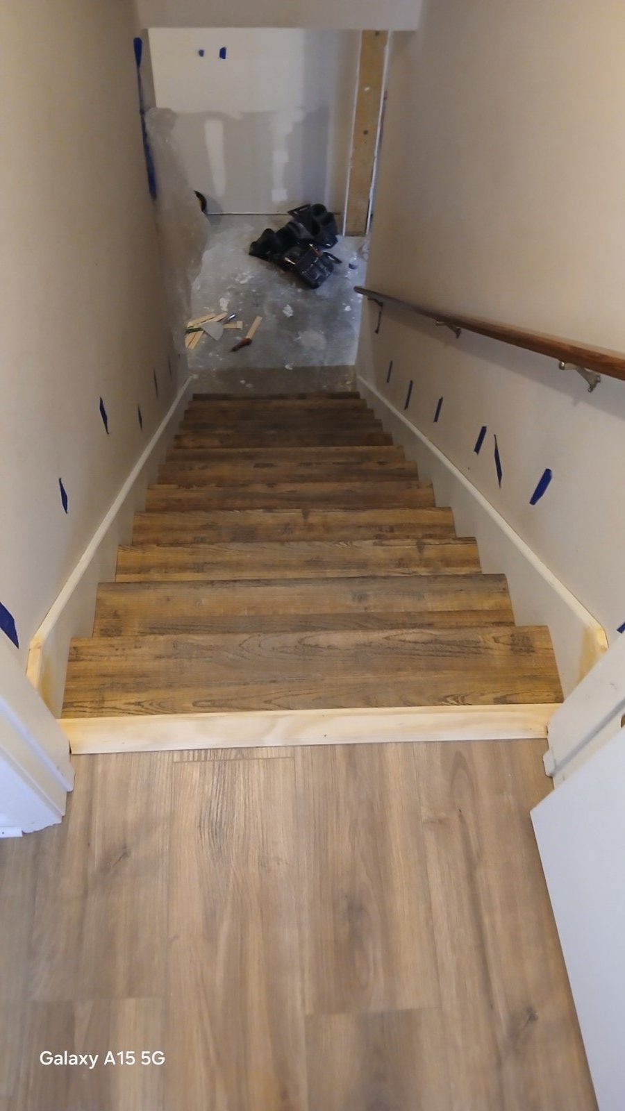 View from top of new basement stair showing stained reclaimed wood treads being set.