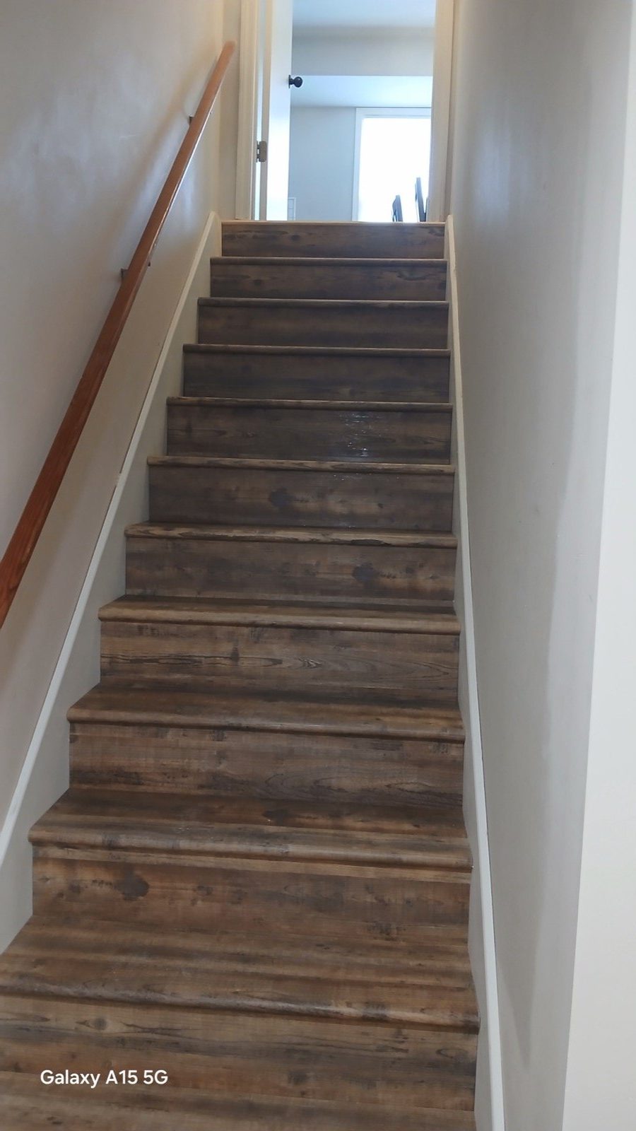 Finished rustic reclaimed wood baluster wall beside new basement stair with vinyl plank floor and painted ceiling.