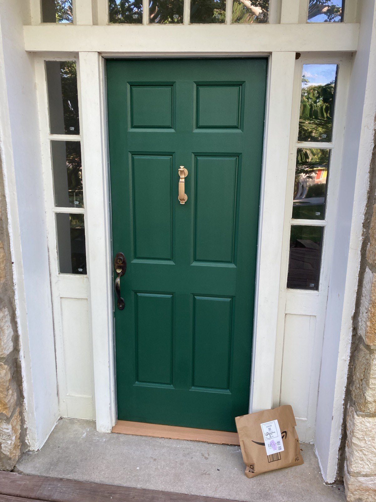 Restored six-panel entry door painted green with brass hardware in stone surround with sidelights and transom