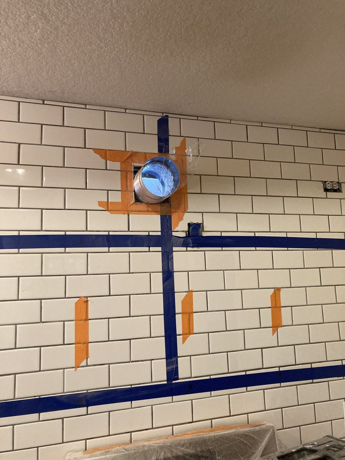 Round vent opening cut through subway tile backsplash, taped off for the range hood duct.