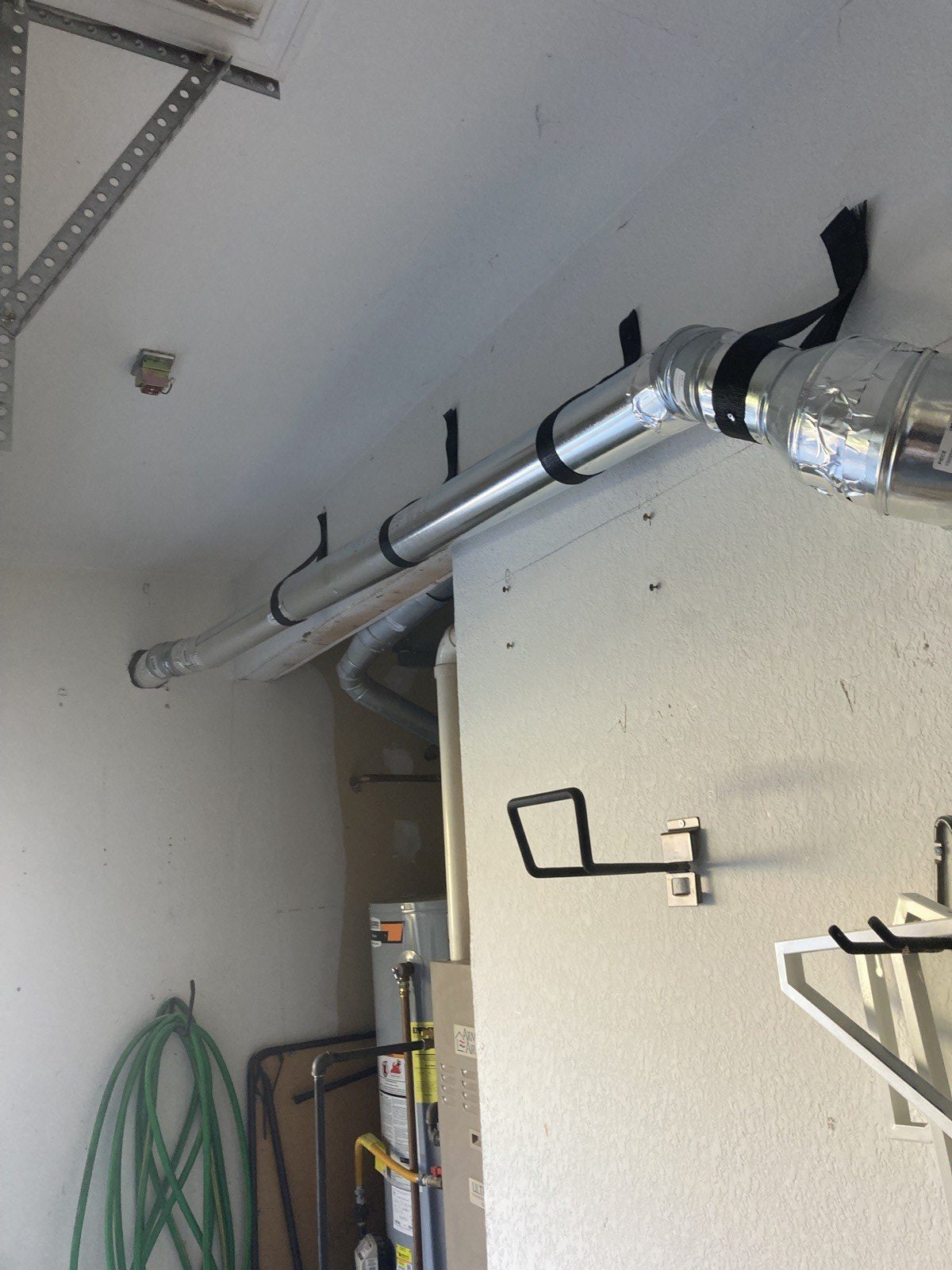 Insulated vent duct strapped along a garage ceiling running toward the exterior wall.