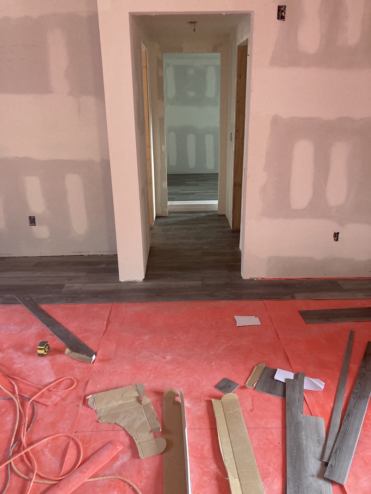 Cut pieces of gray vinyl plank flooring staged on red protective paper in a hallway.